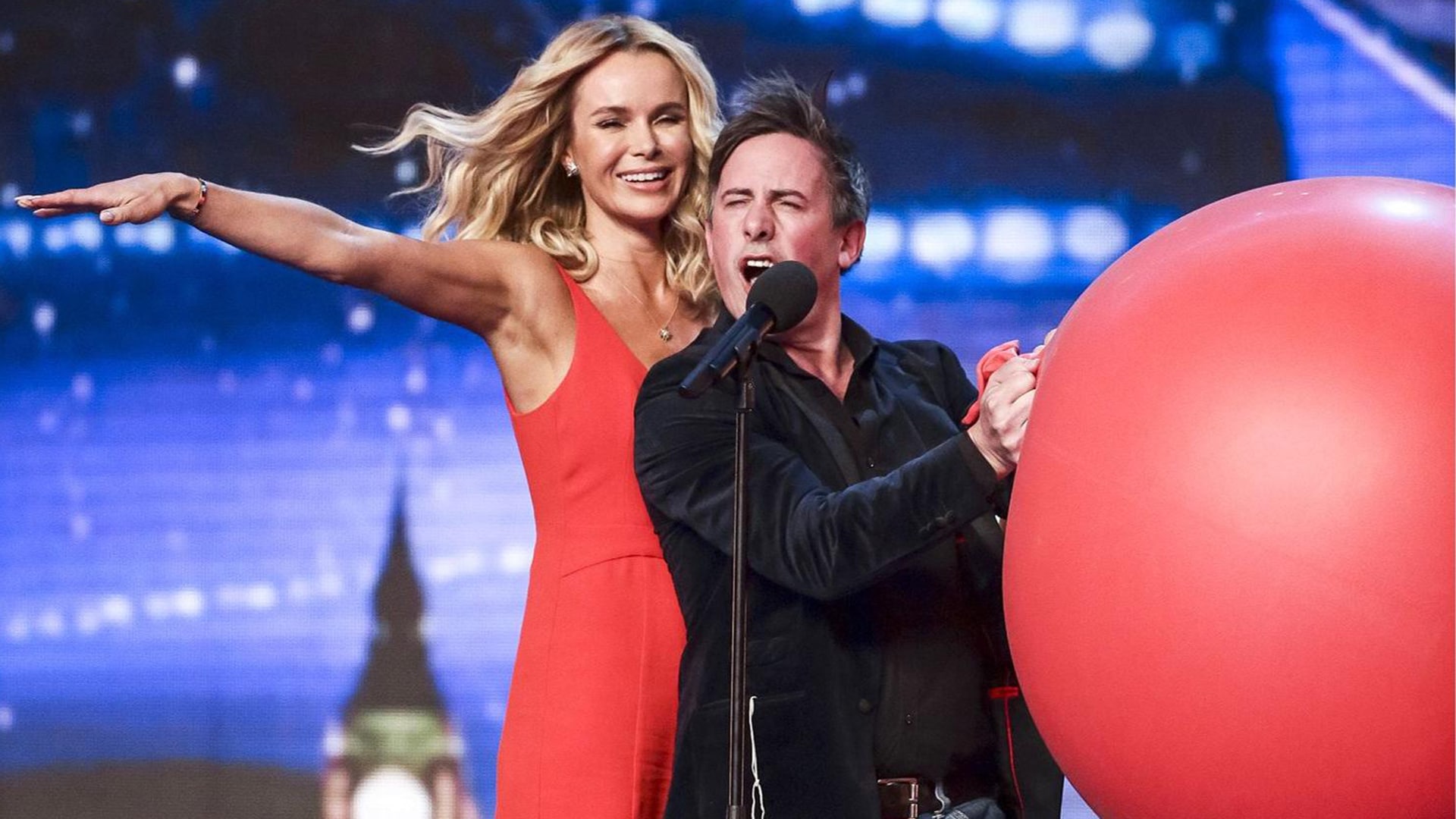 Christian Lee performing in Britain's Got Talent, standing next to Amanda Holden while holding a massive red balloon