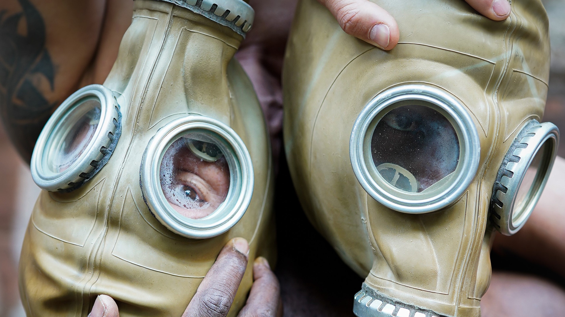 two performers wearing gas masks - grasping each other's masks