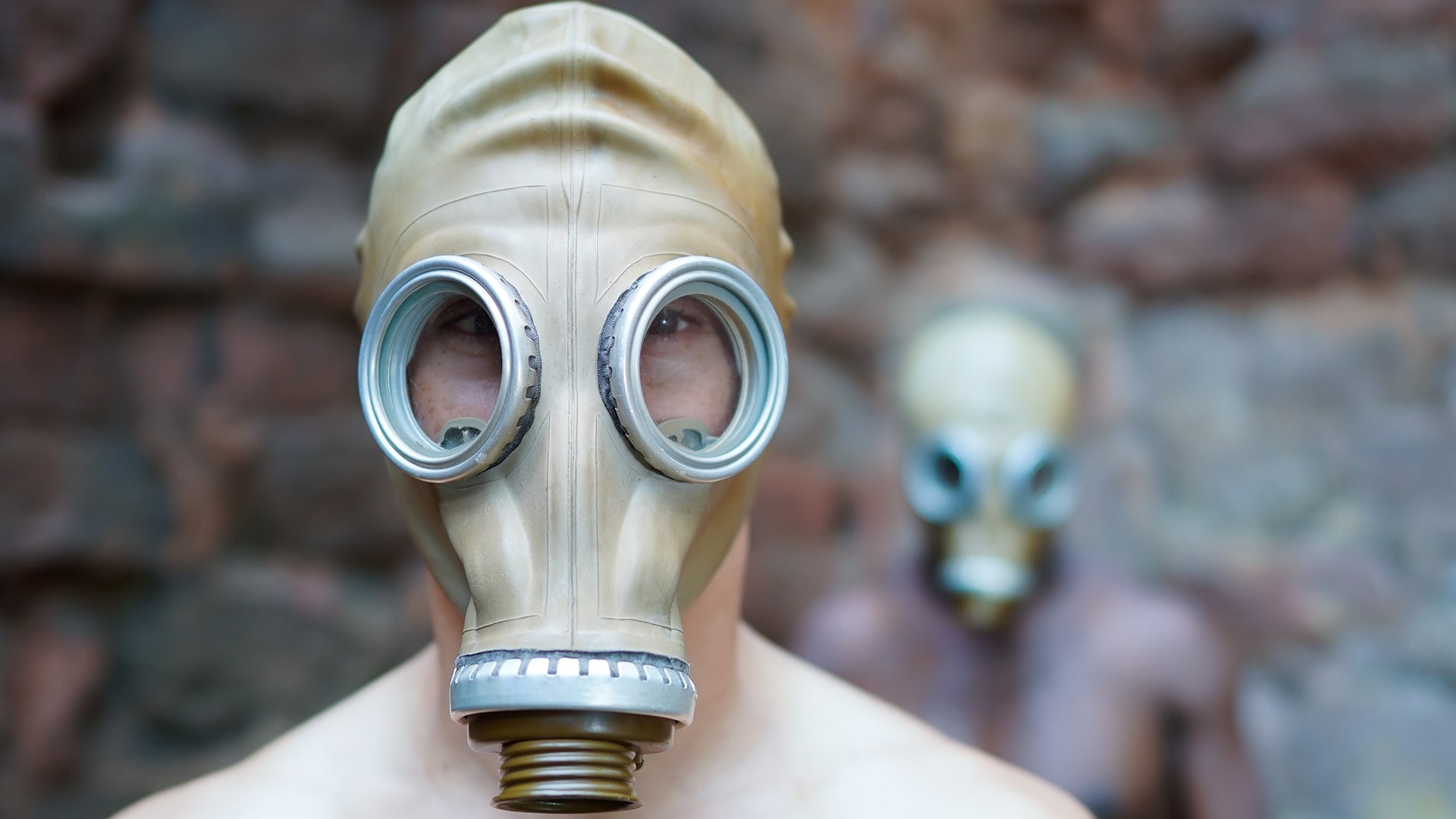 two performers wearing gas masks - one standing in front of the other