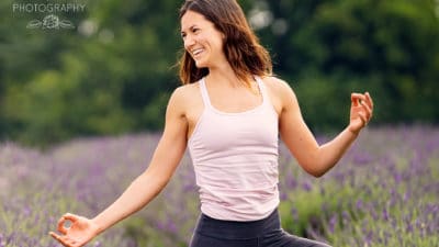 Woman practices a yoga pose in a field of lavender. One arm is bent, the other outstretched