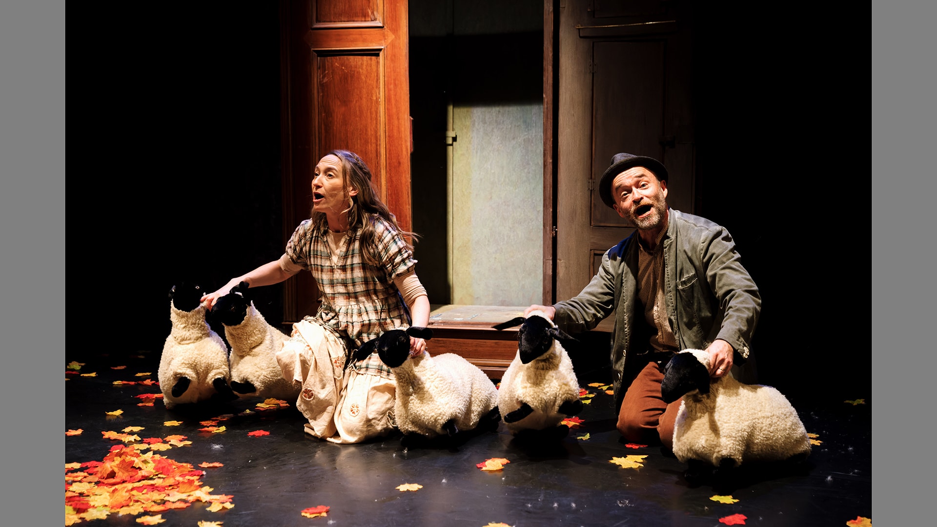 A man and woman kneel down on a stage surrounded by five puppet sheep
