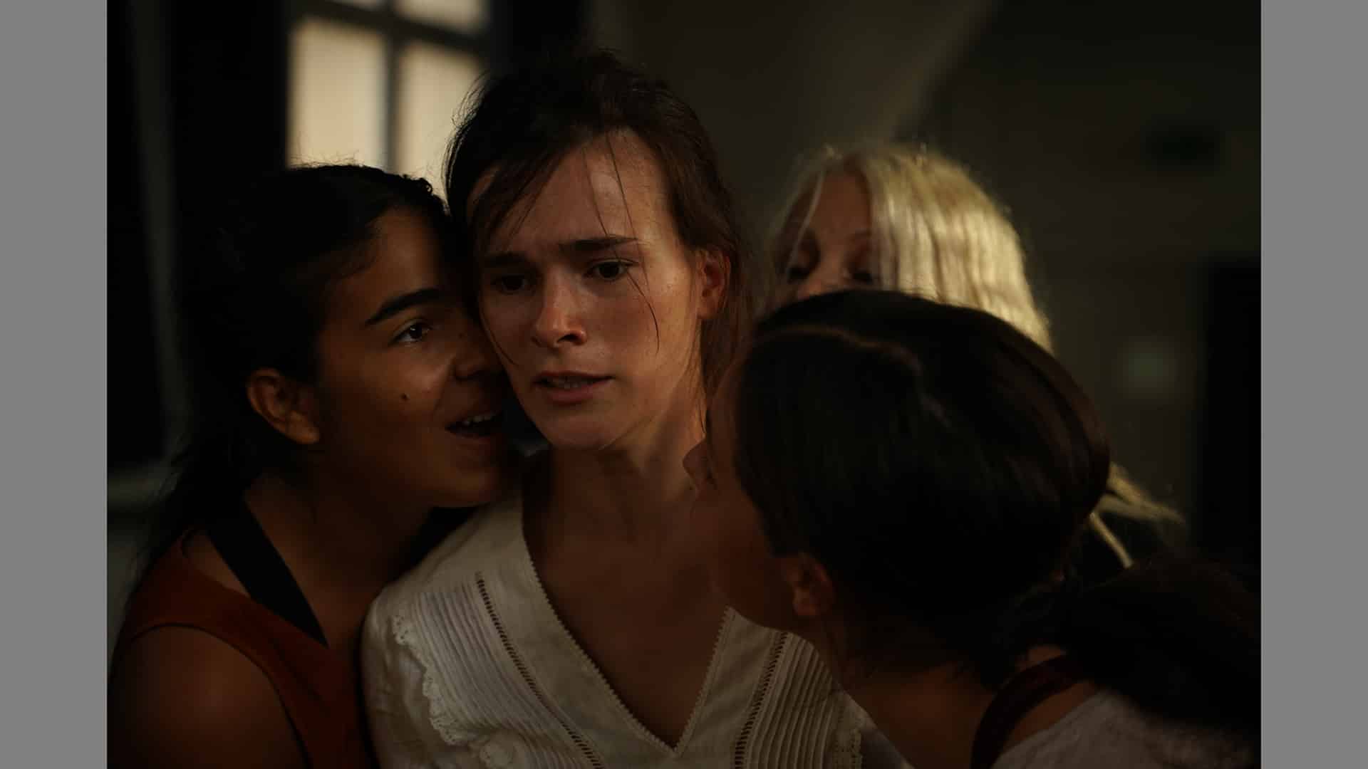 A grounp of three women gather around a central woman who looks shocked