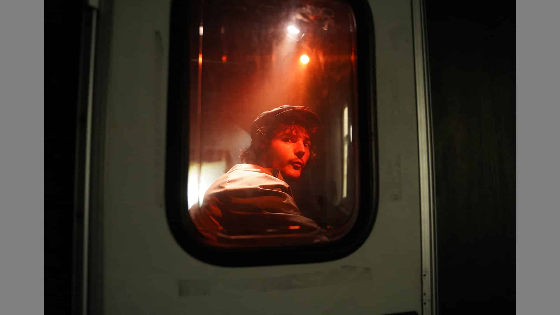 Person bathed in red light looks over their shoulder, out of a window