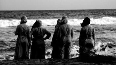 Four nuns stand on the beach looking out into the ocean