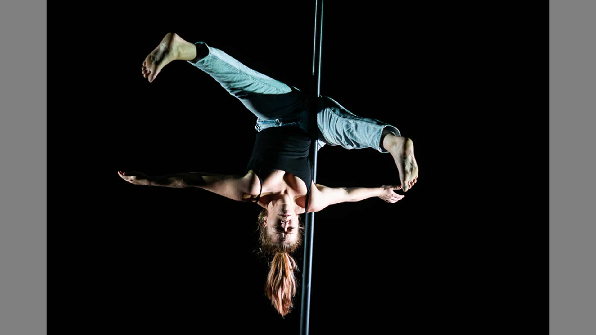 A performer hangs upside down on a Chinese pole, their arms and legs extended out like a starfish