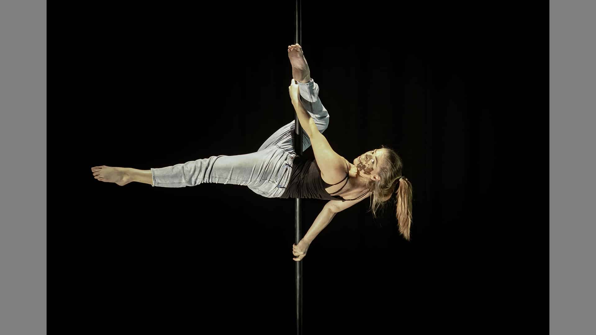 A performer holds themselves horizontally off a Chinese pole