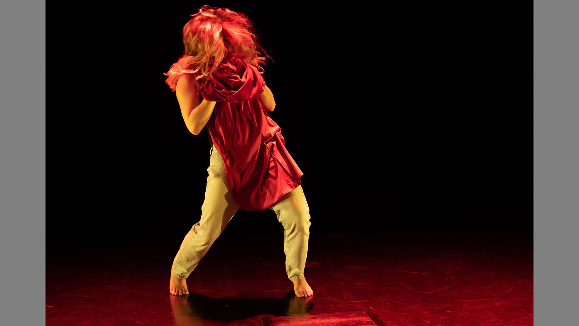A performer clutches a piece of red fabric to their chest. Their face is obscured by a red wig