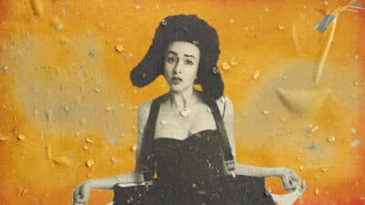 Julia is pictured in black and white against a distressed orange background. She's wearing a fur hat with ear flaps. Her fingers are plucking out the lining of her pockets to show they are empty