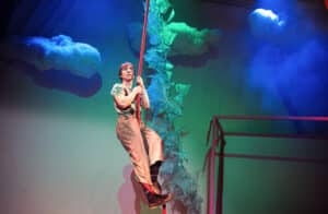 The actor playing the giant is climbing up the rope representing the beanstalk. He gazes out into the distance.