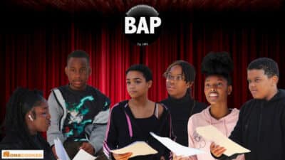 Six Global Majority performers are pictured in front of a red curtain. They each hold scripts in their hands. Above them is the BAP logo