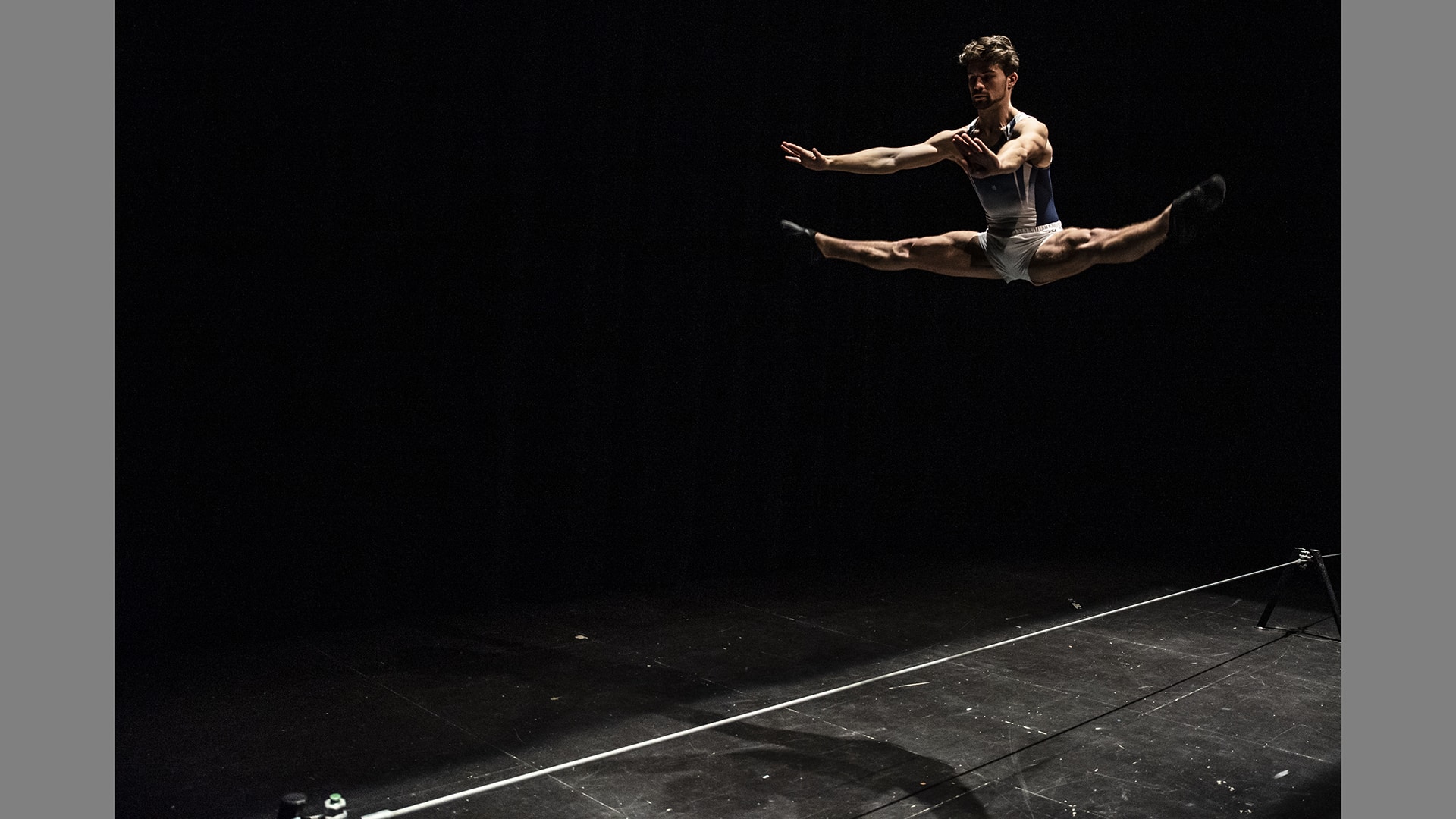 Circus artist Simon-James jumps high, his legs out in a split. He is high above the stage