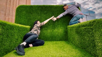 A huge grass armchair fills the frame. On one side sits a woman. She reaches out to a man who is perched on the arm of the chair