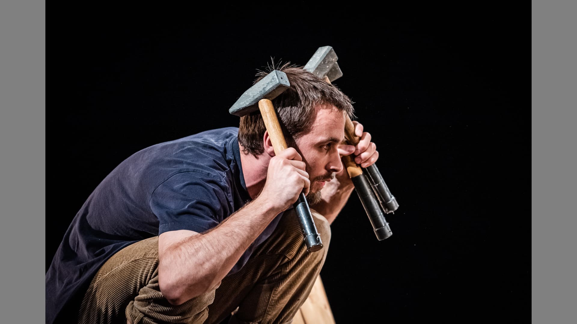 A performer crouches and holds up hammers to cover his ears