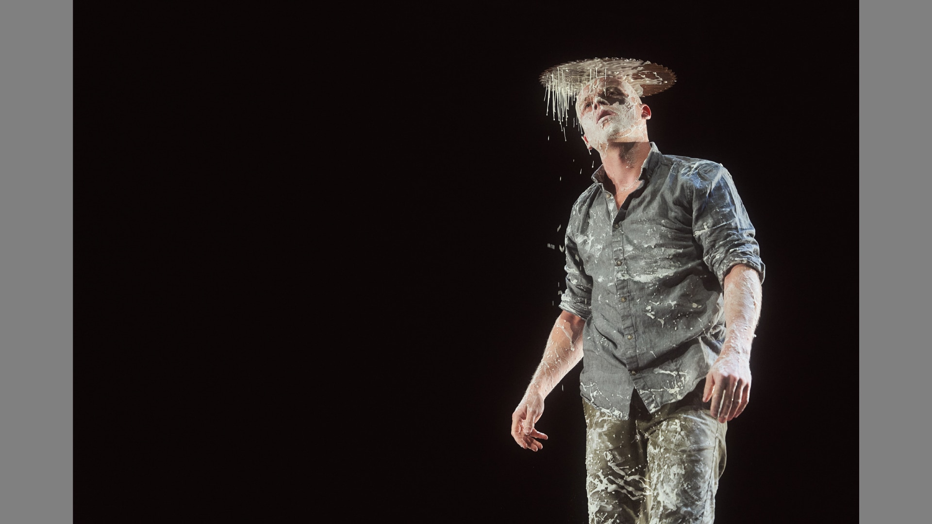 A performer balances a circular saw blade on his head. He's covered in white glue