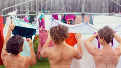 A photo of three woman pinning up laundry outside. They appear nude, but we only see their backs