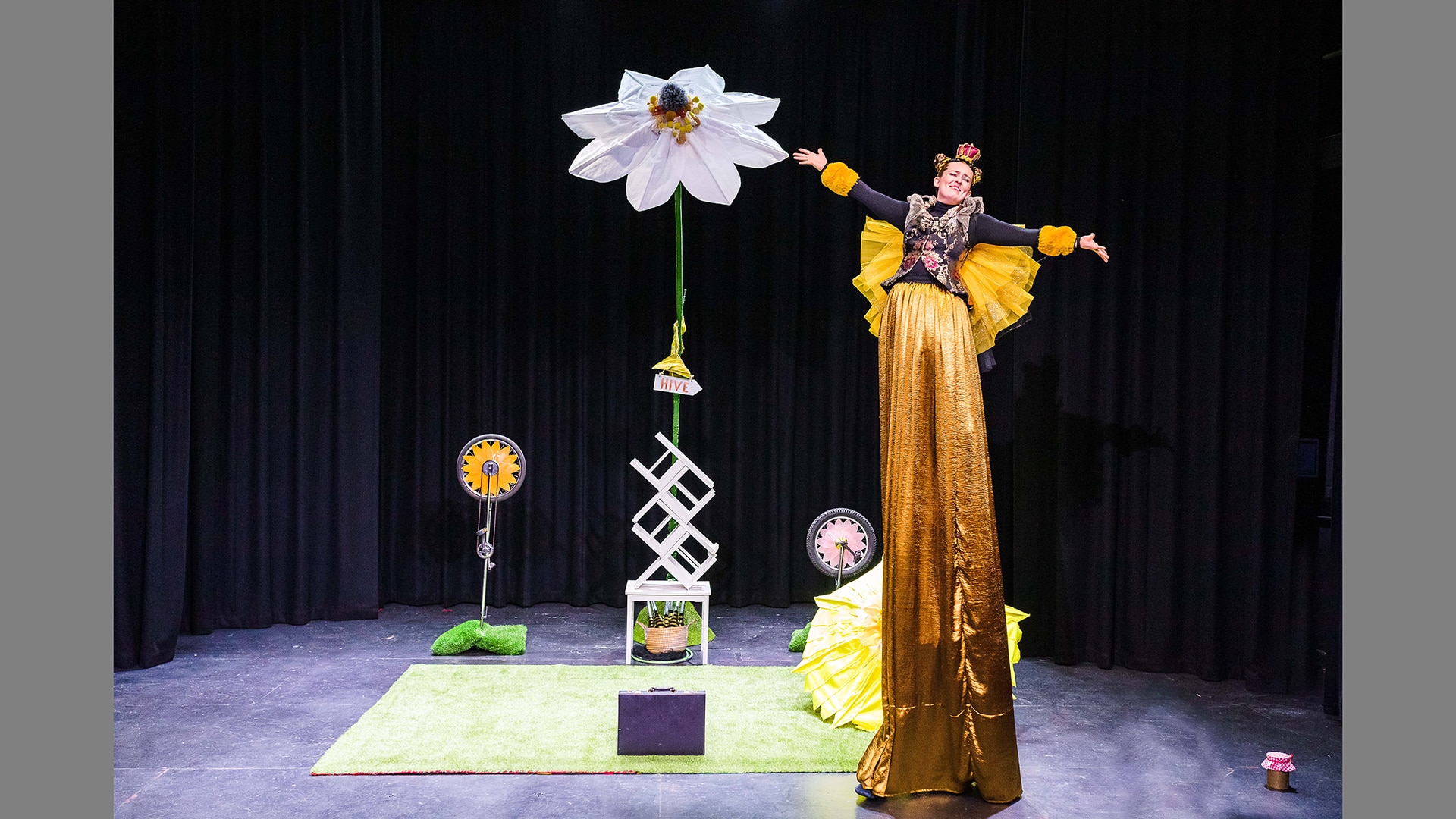 A performer stands on stilts covered in magnificent golden trousers and shows off her wings