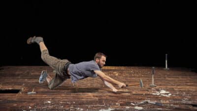 A performer throws themselves across the stage as they attempt to hit a nail into the floorboards