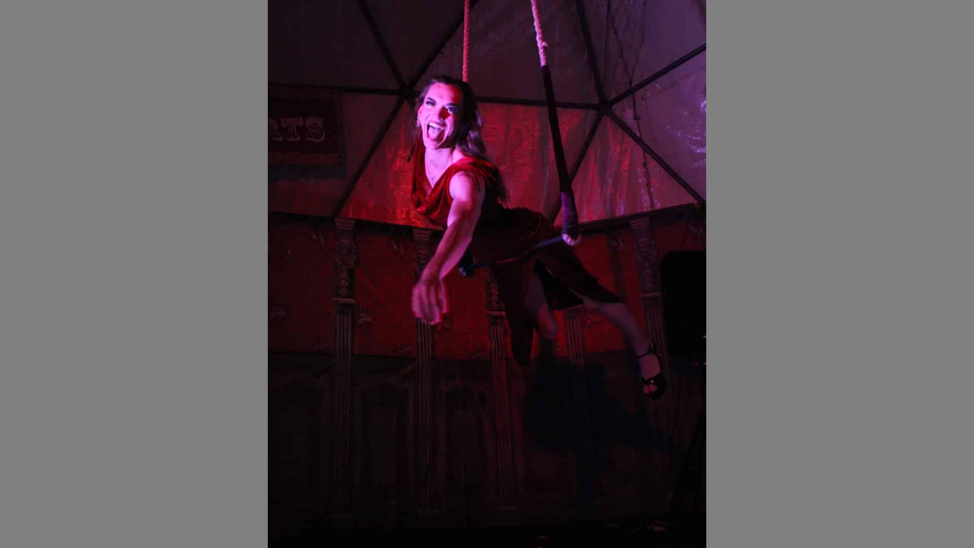 A woman swinging on a trapeze reaches out to the viewer