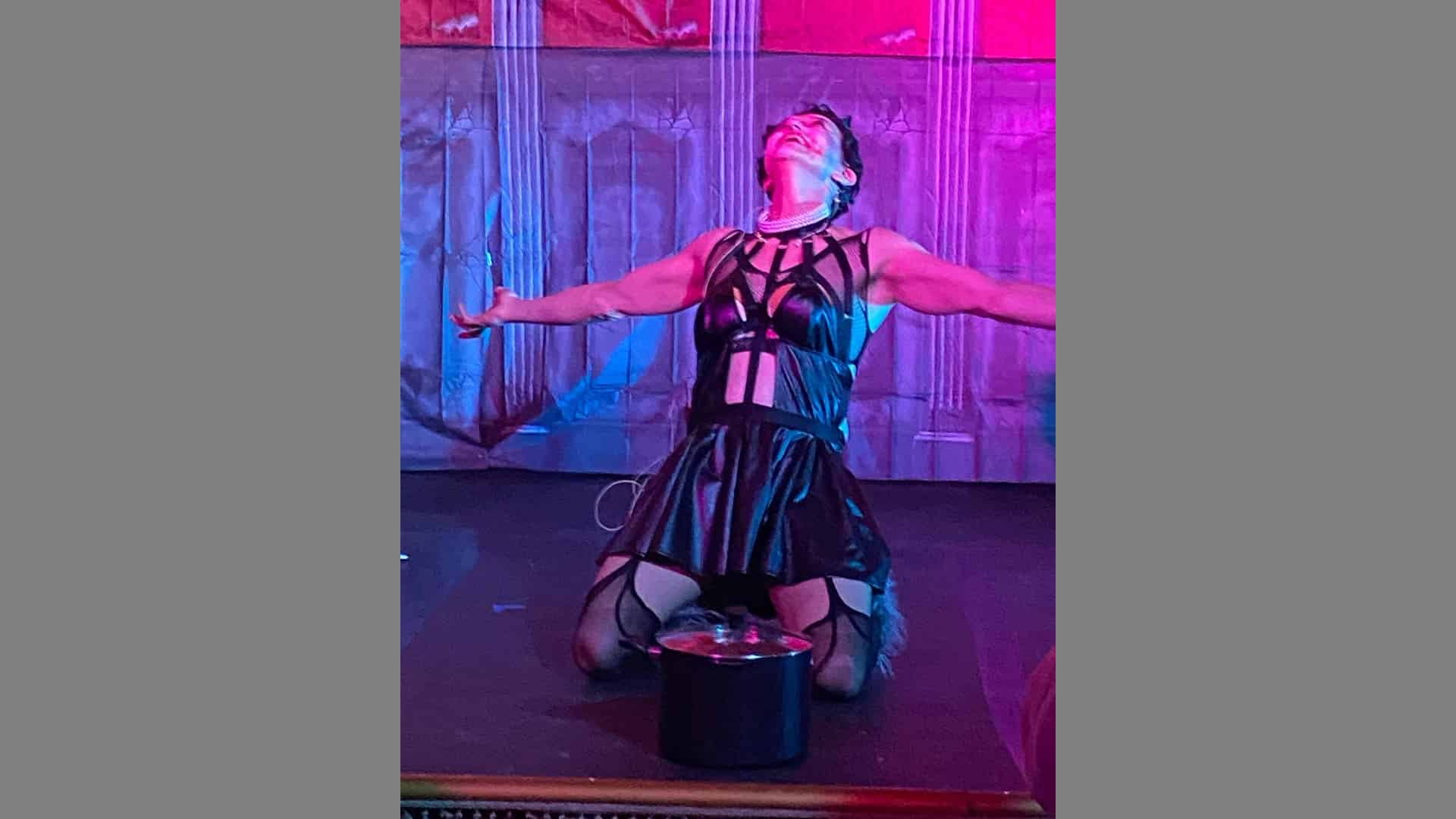 A performer kneels on the stage, wearing garters and a corset