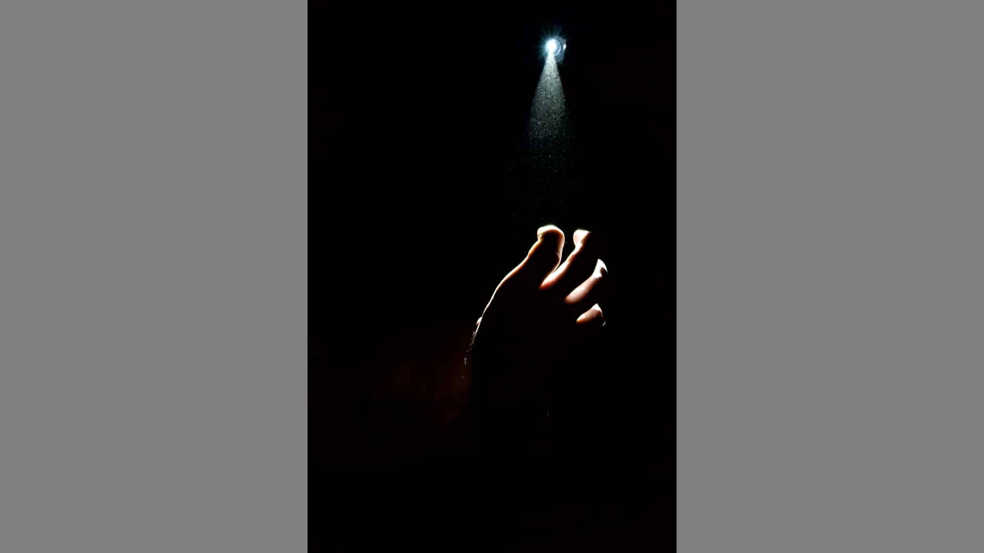 A hand reaches out of the darkness towards a light