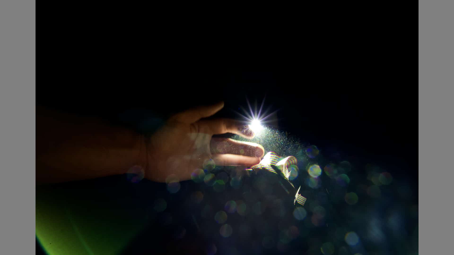 A hand reaches through the darkness to touch a spark of light