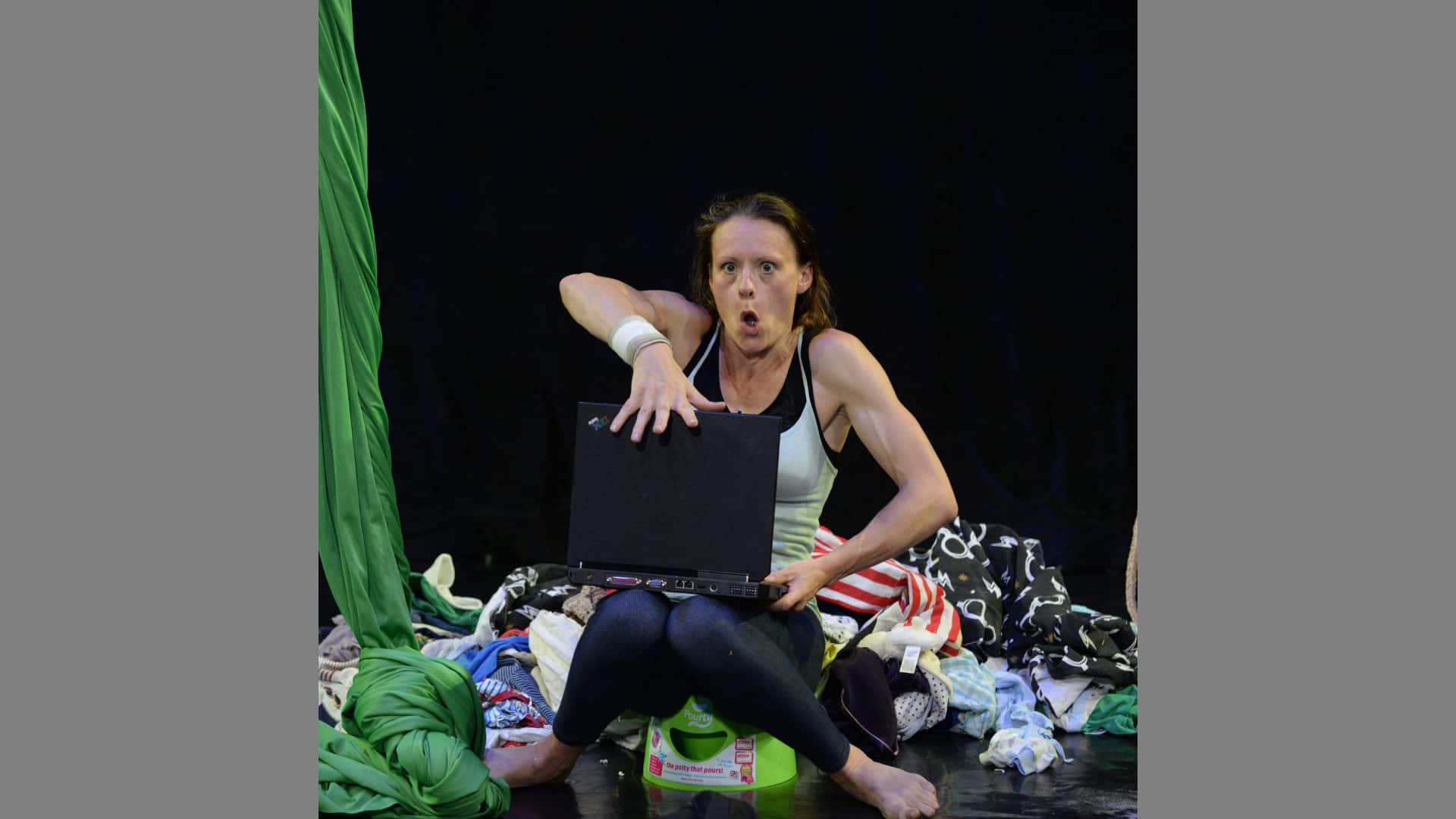 The performer makes to slam down the lid of her laptop. She is surrounded by piles of laundry. Her mouth forms a perfect o of exclamation