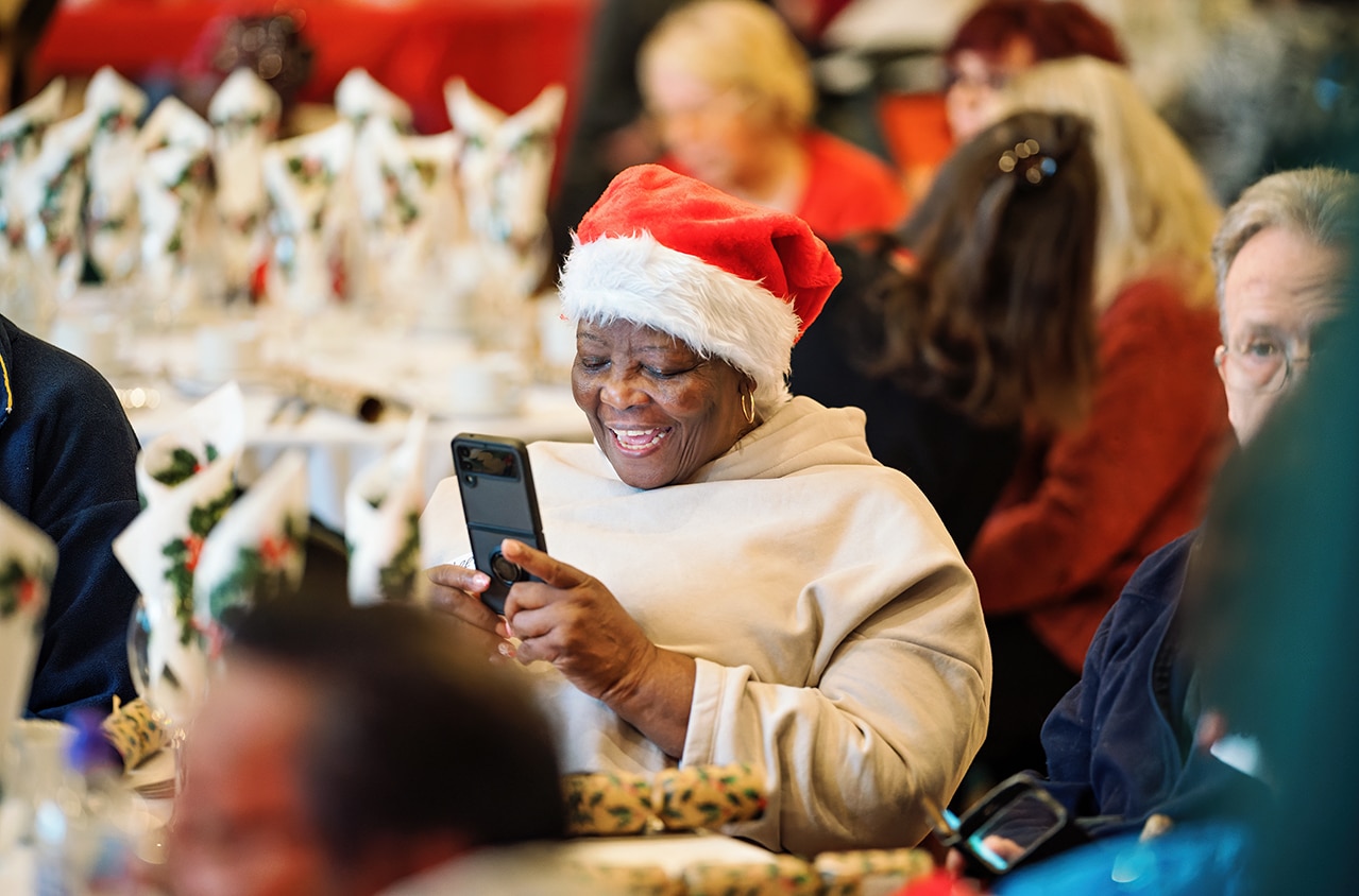 A black woman wears a santa hat laughing at her phone at the christmas day event