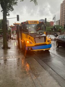 A yellow school bus waits on the side of pavement slick with rain