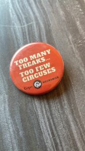 A small orange badge, with text in white reading: Too many freaks... Too few circuses