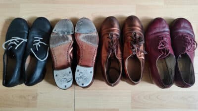 Four pairs of tap shoes are lined up on a wooden floor
