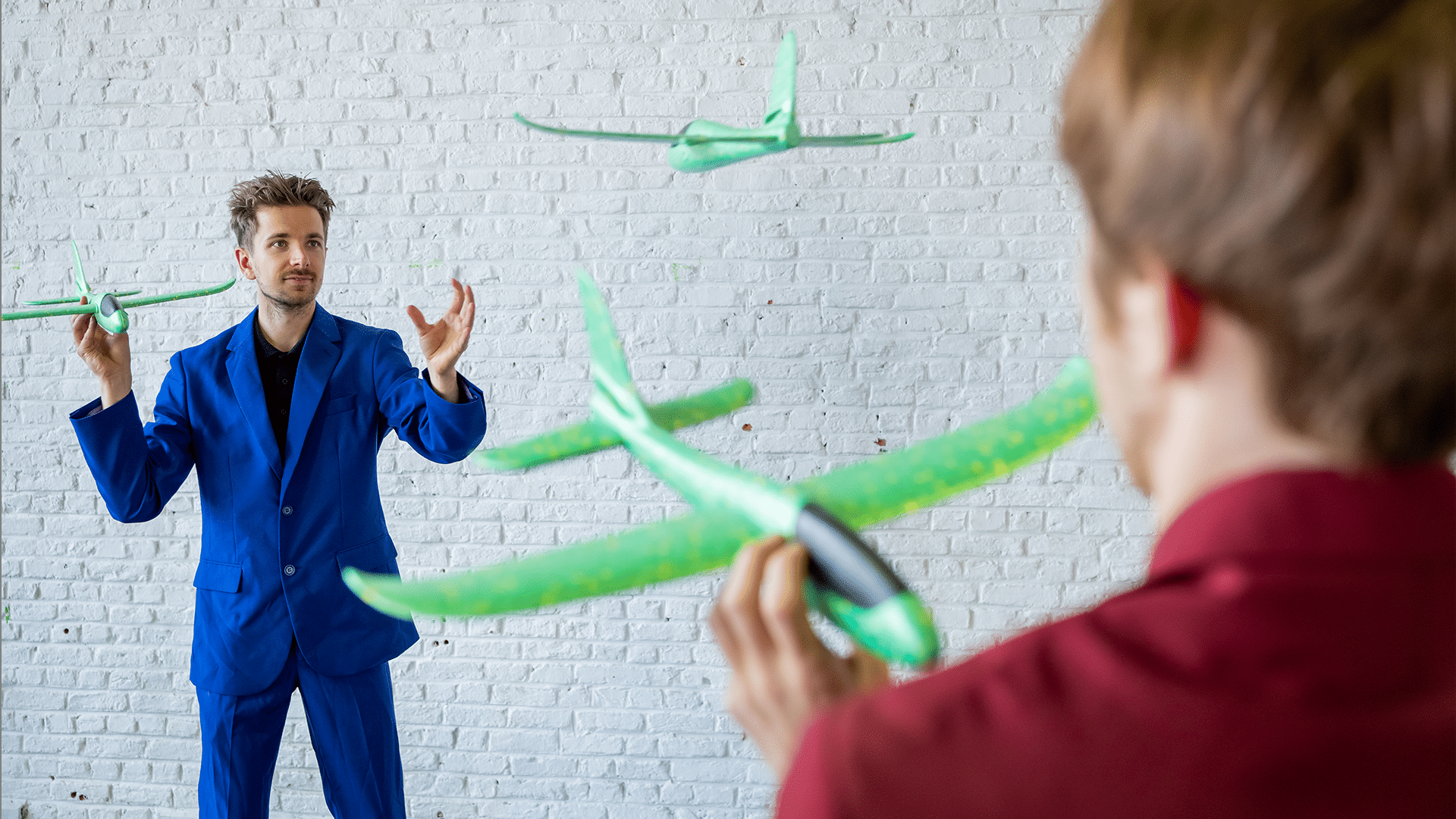 Two performers throw green miniature aeroplanes between each other.