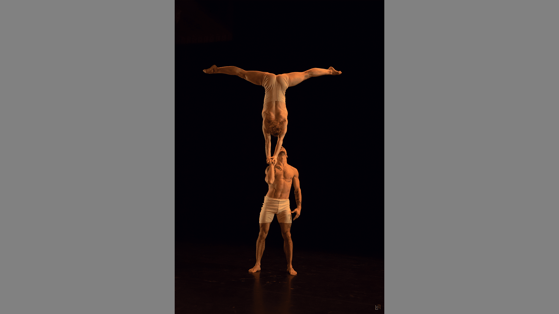 One acrobat holds another in a handstand with one arm.