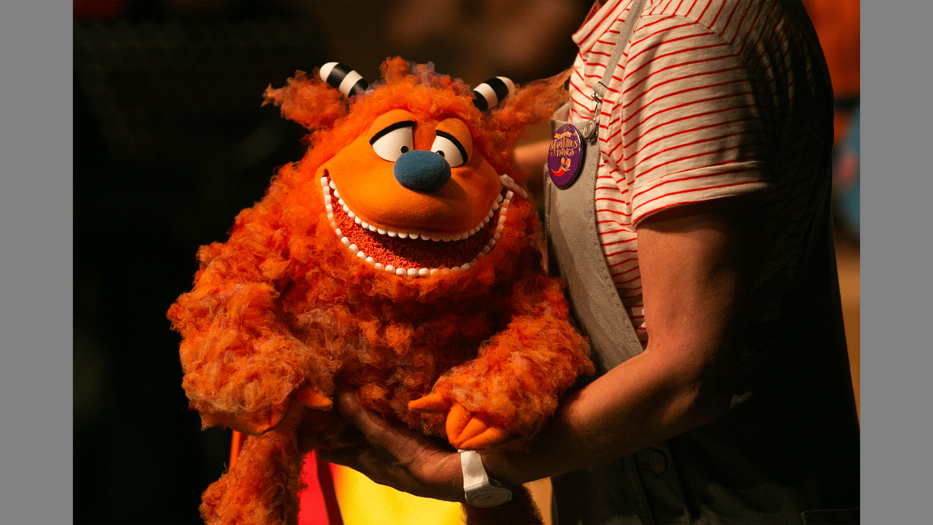 A muffle wumper looks at the camera, he has furry orange hair, a blue nose, and black and white stripy horns.