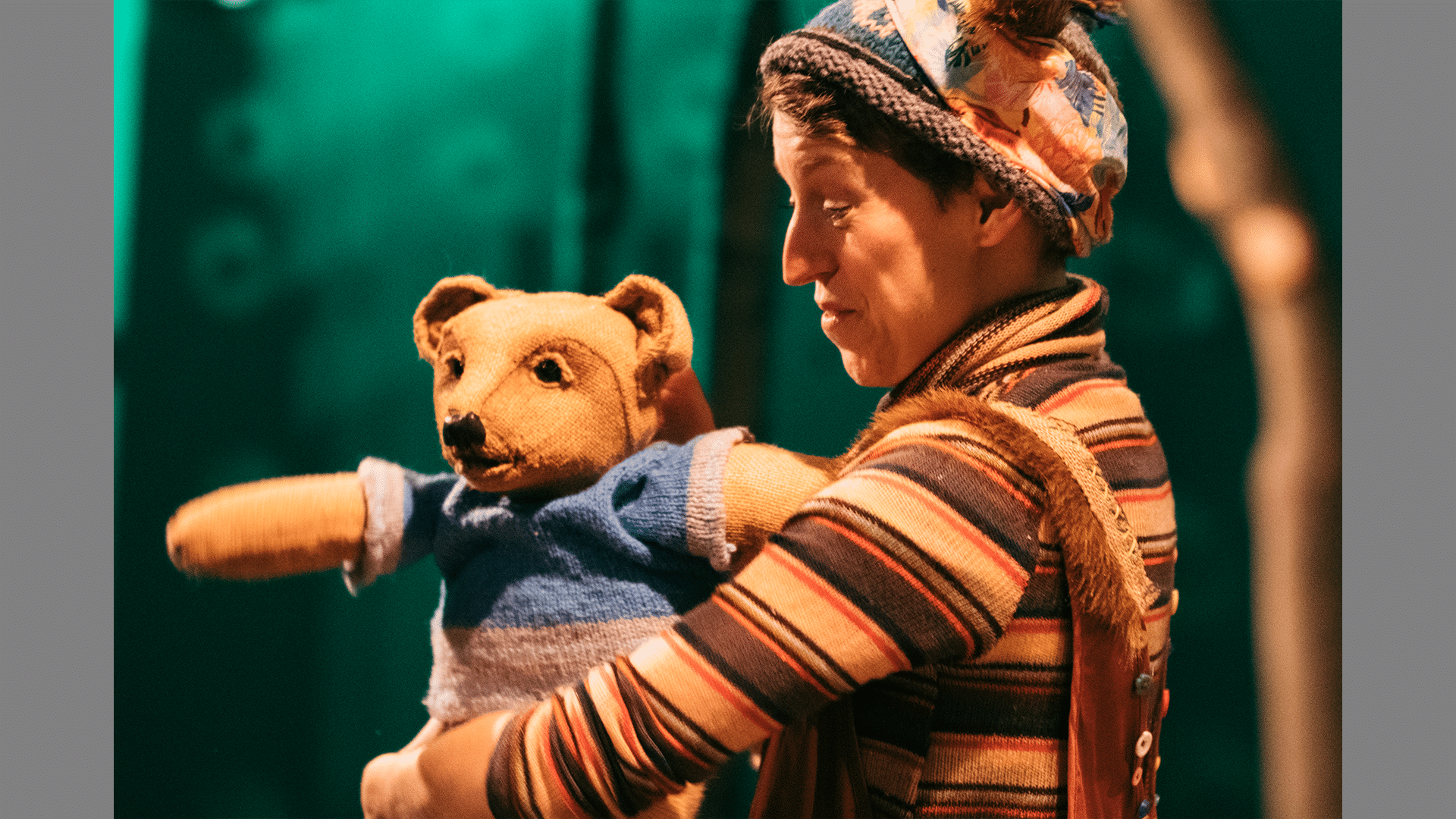 A performer stands on stage holding a baby bear puppet, they look at it happily.