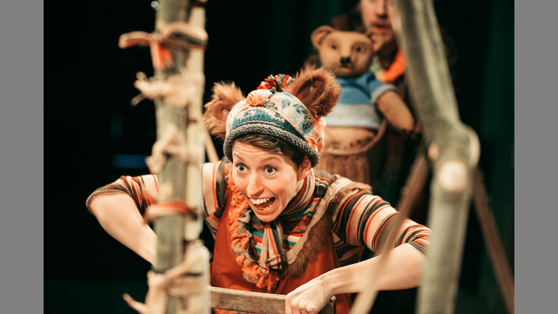 A performer stands on stage wearing a knitted hat with bear ears on, they look excited.