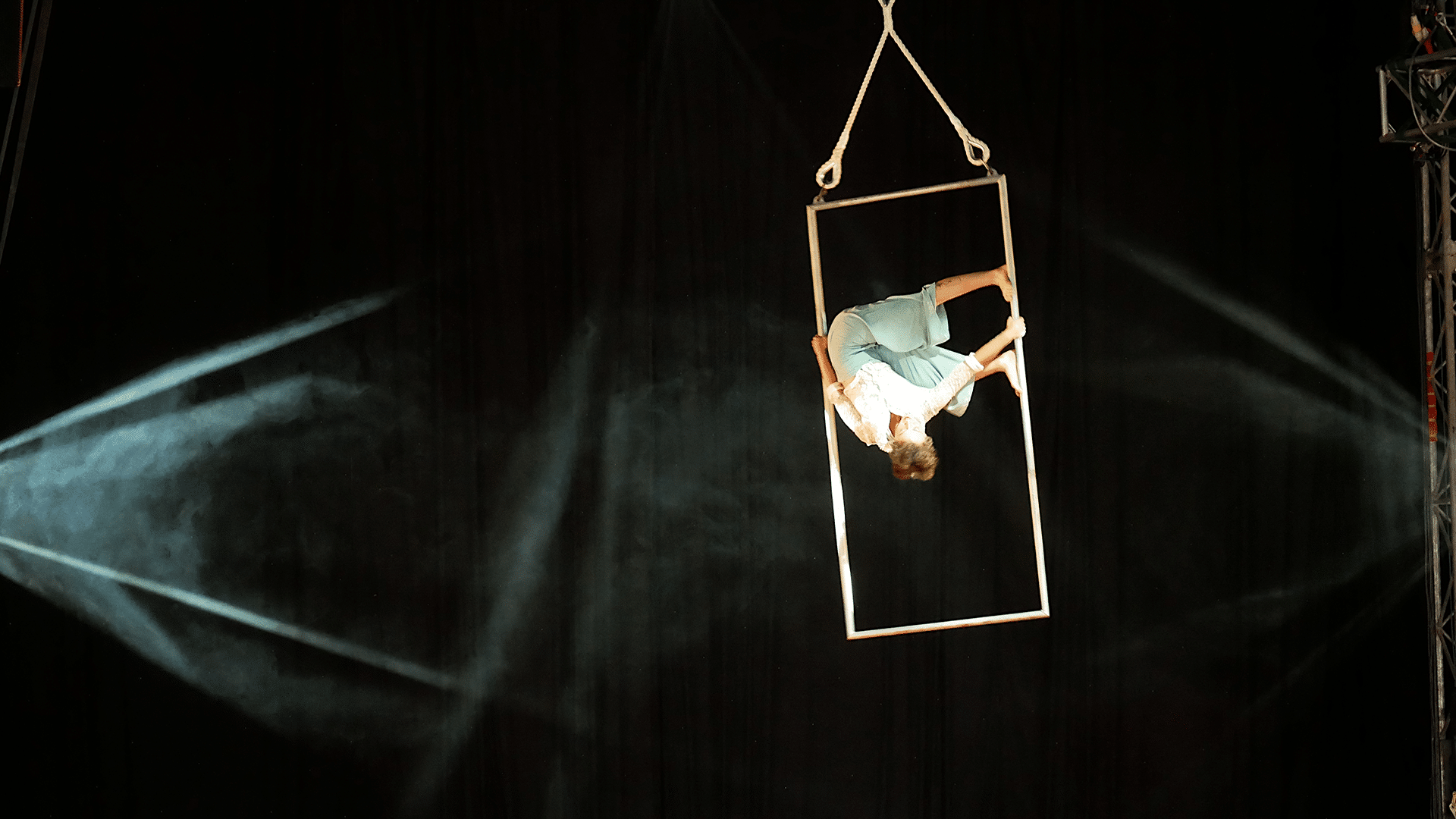 A circus artist performs an upside down move on a piece of aerial equipment.